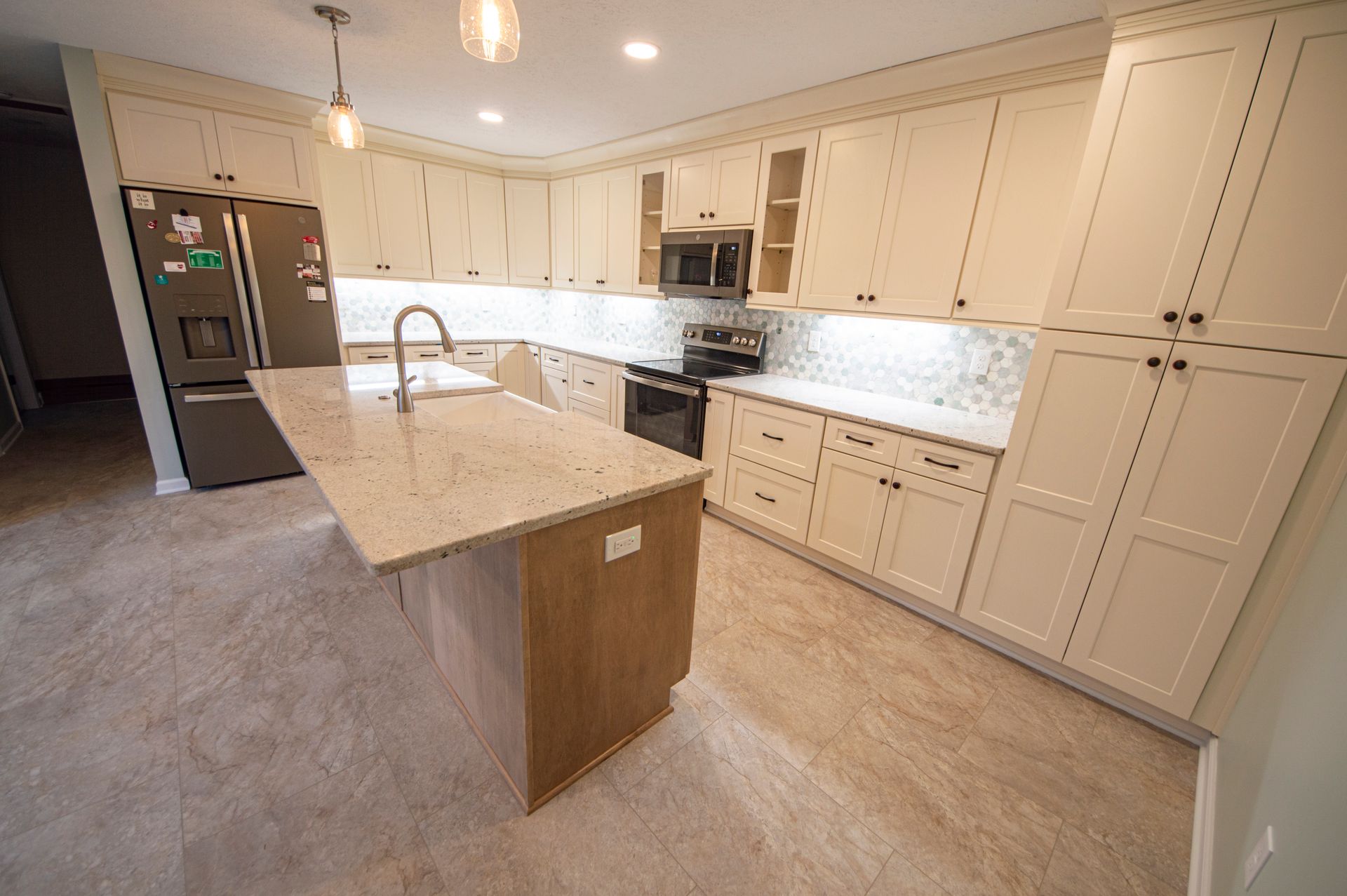 Cream-colored kitchen with a large island, stainless steel appliances, and light-colored countertops and cabinets.