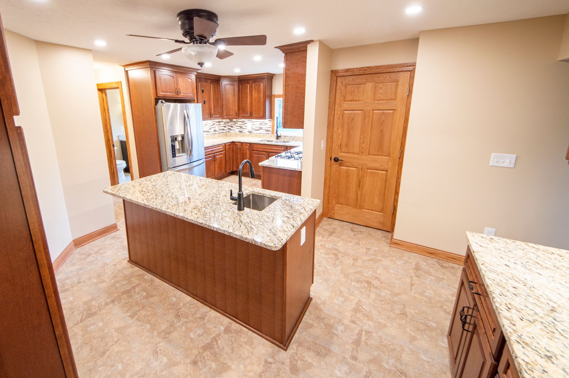 Kitchen with brown cabinets, granite countertops, island with sink, and tile floor.