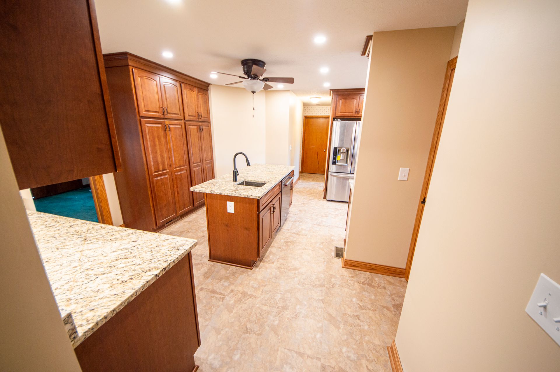 Kitchen with wooden cabinets, island, stainless steel refrigerator, and tan flooring.
