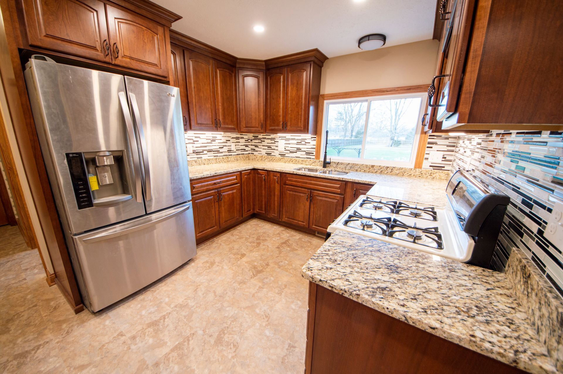 Kitchen with stainless steel refrigerator, brown cabinets, granite countertops, and tile backsplash.