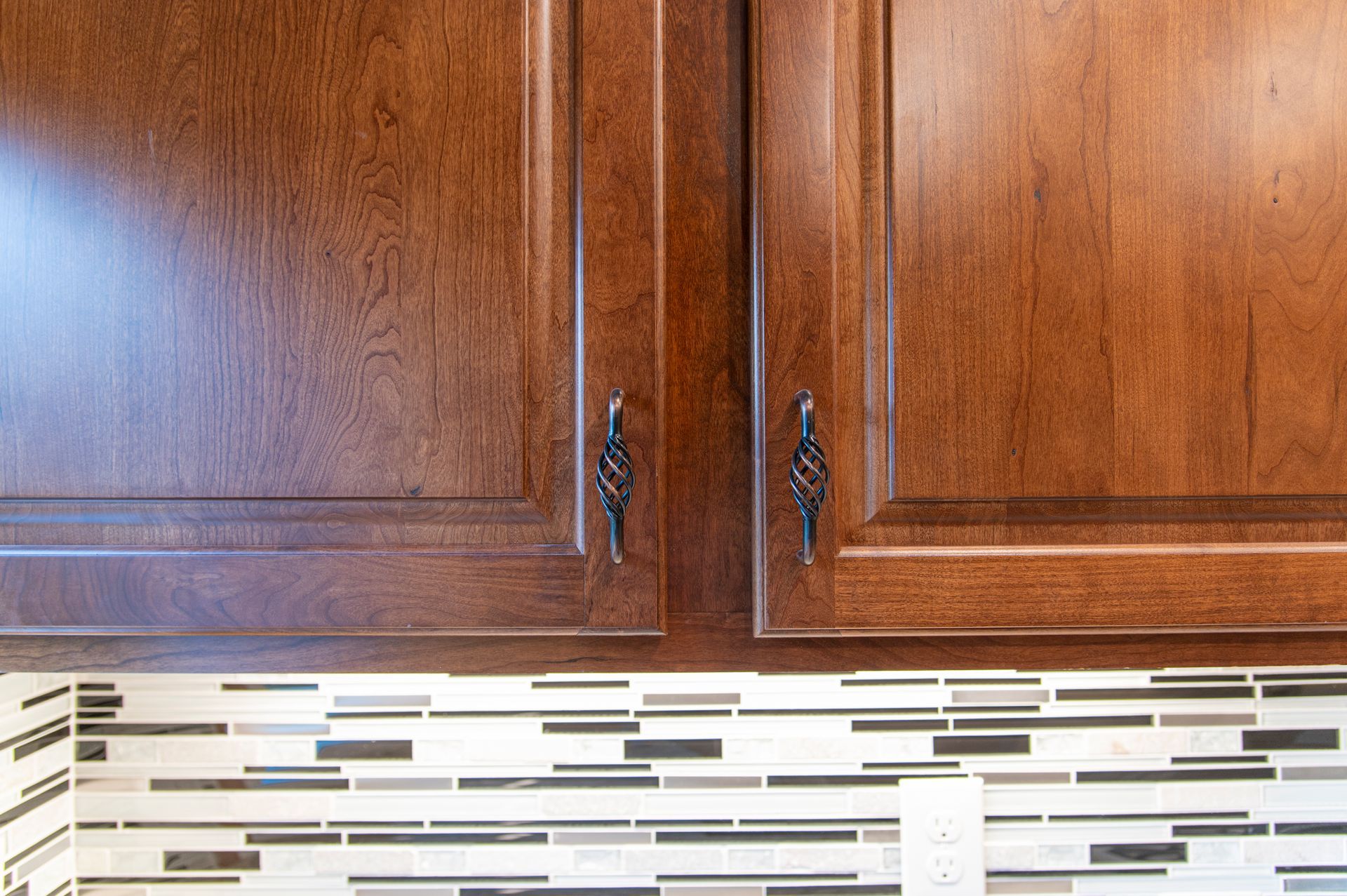 Brown kitchen cabinets with ornate black handles above a tiled backsplash.