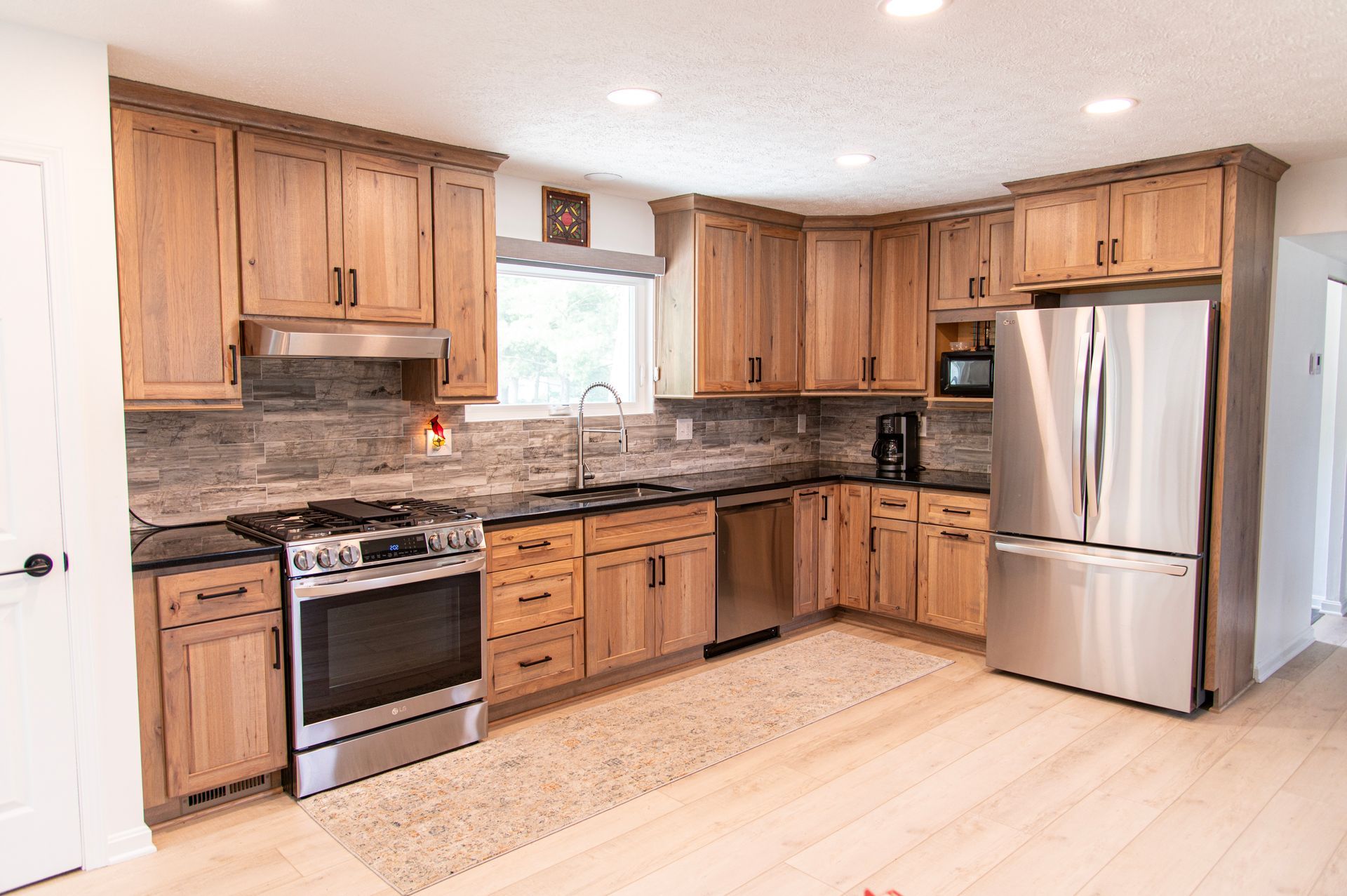 Wooden kitchen with stainless steel appliances, dark countertops, and light-colored flooring.