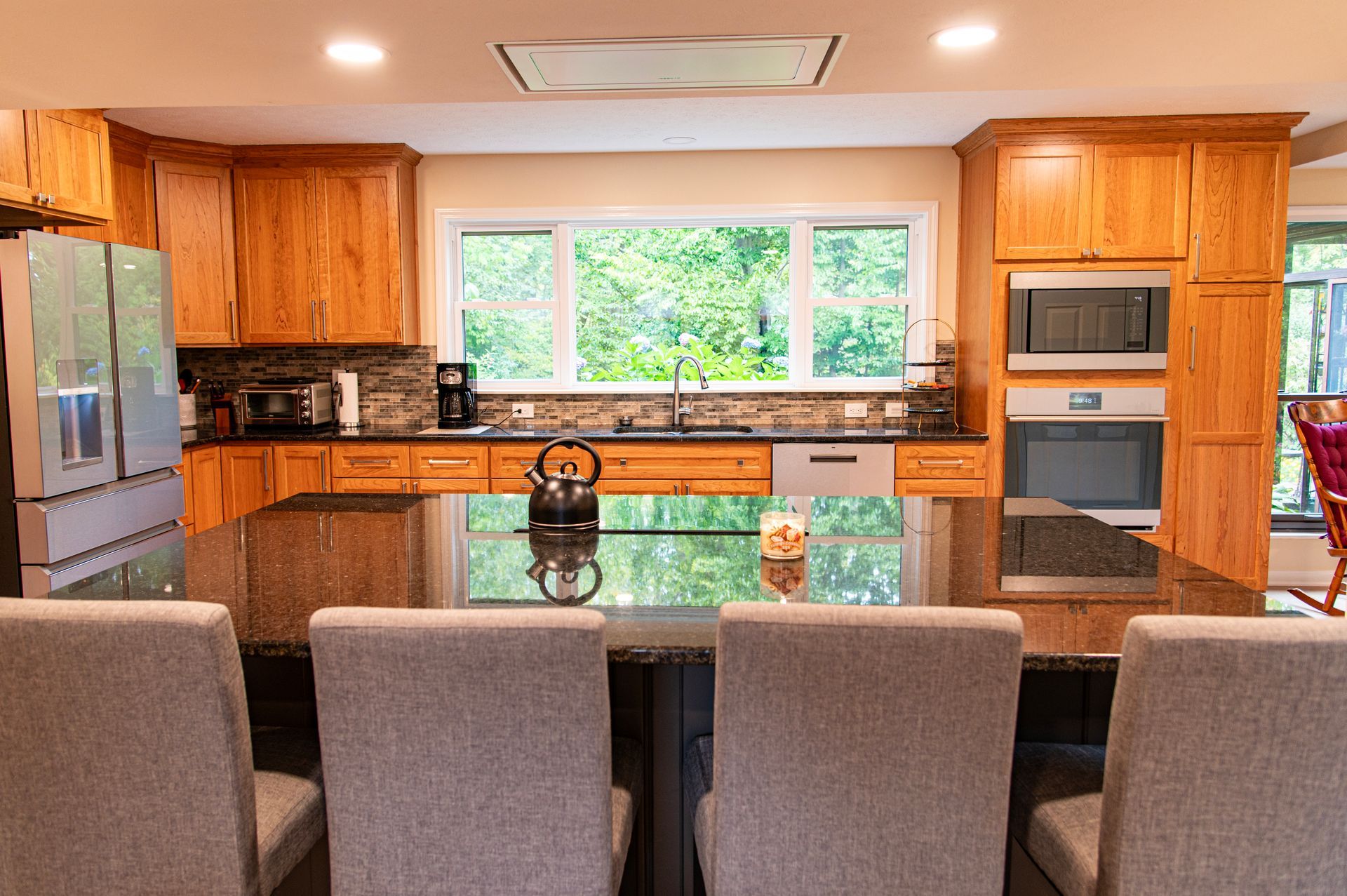 Kitchen with island seating, bamboo cabinets, black countertop, and large window overlooking greenery.