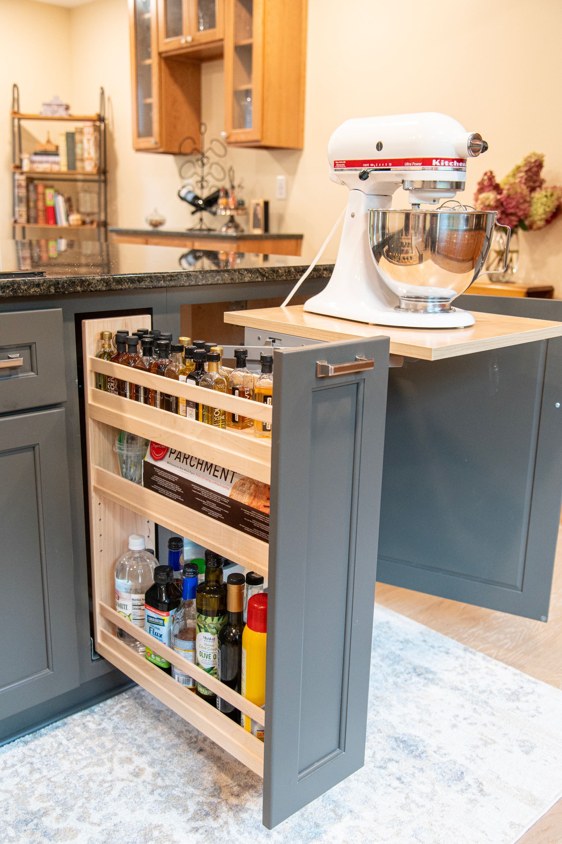 Gray pull-out spice rack next to an island counter with a stand mixer. Kitchen setting.