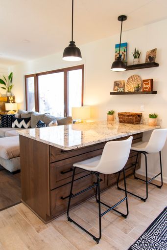 Kitchen island with granite countertop, wooden cabinets, and white bar stools; two black pendant lights hang above.