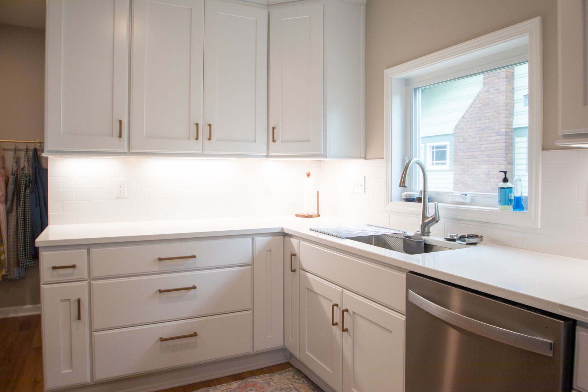 White kitchen with white cabinets, countertops, and a stainless steel dishwasher.