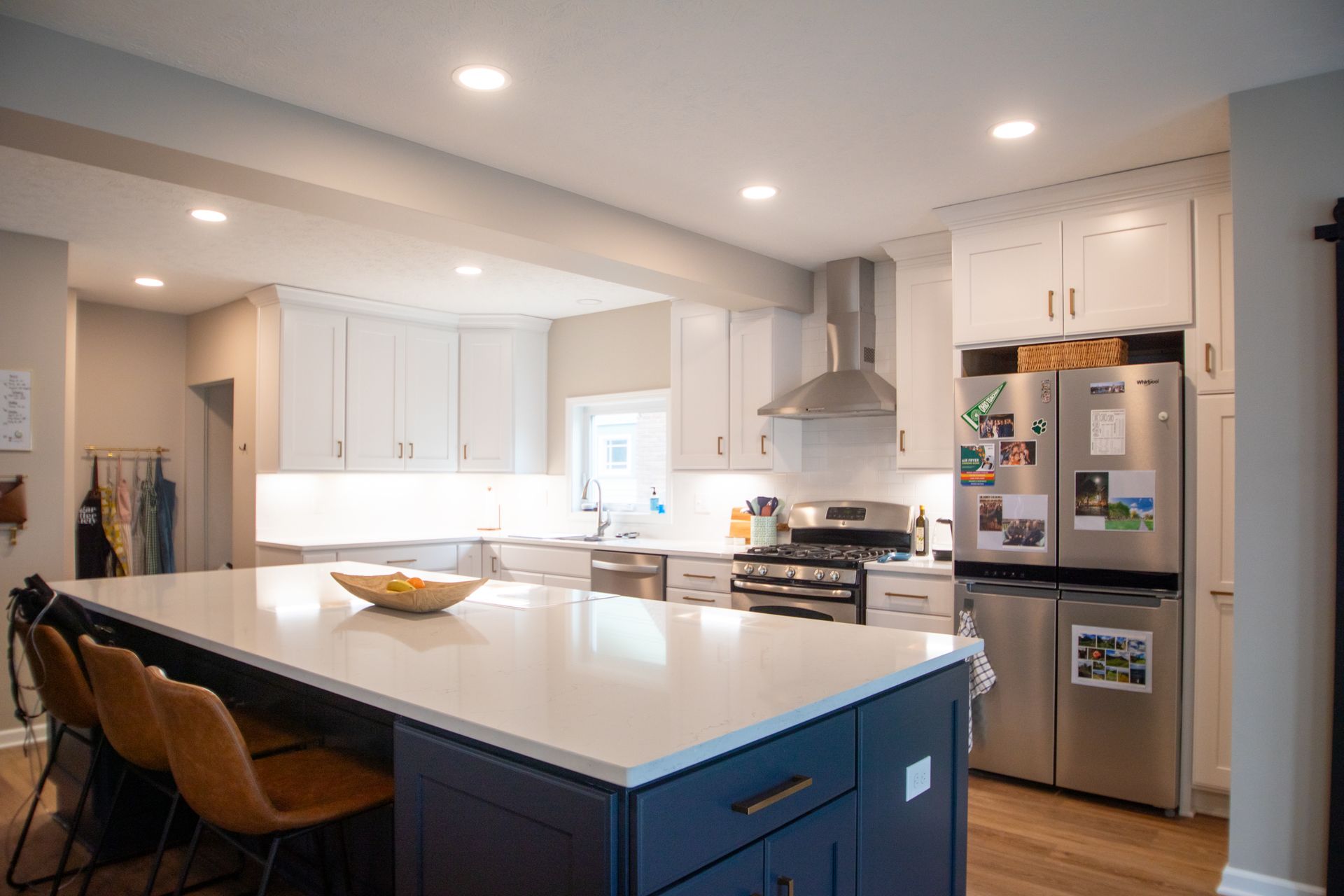 Modern kitchen with white cabinets, blue island, stainless steel appliances, and wood floors.
