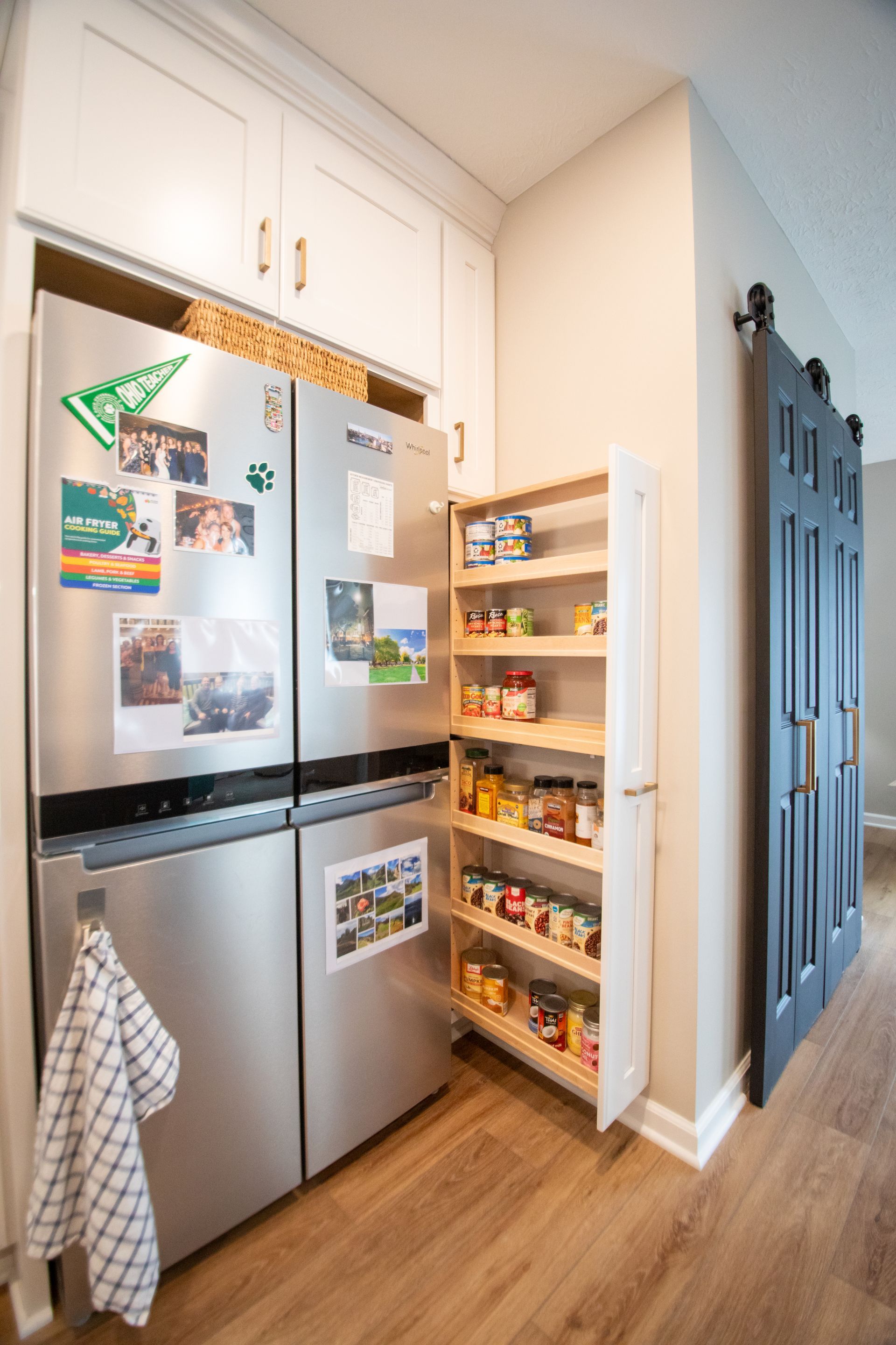 Stainless steel fridge with a pull-out pantry. Kitchen with a sliding barn door, and wooden shelves.