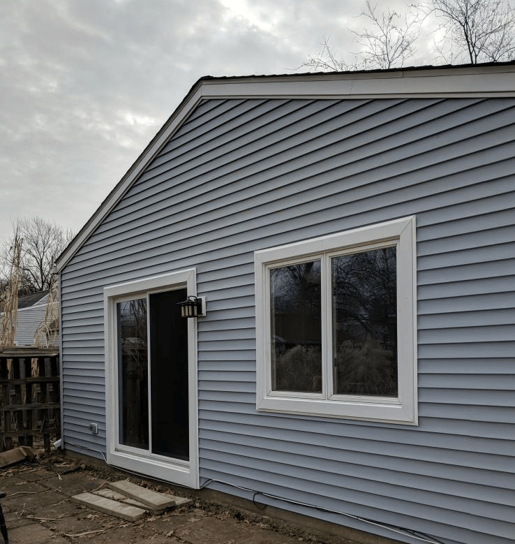 Blue-sided house with a sliding glass door and window. Cloudy day.