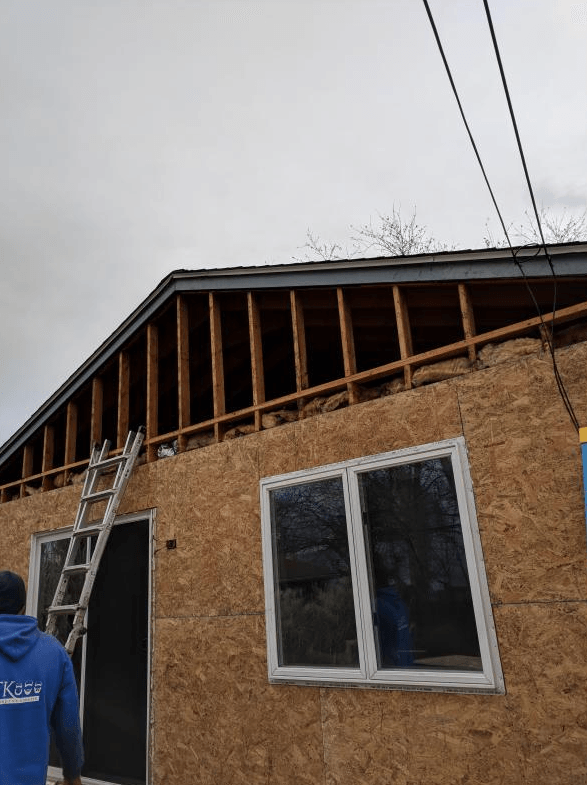 Construction site. House under renovation; exposed rafters. Worker on ladder.