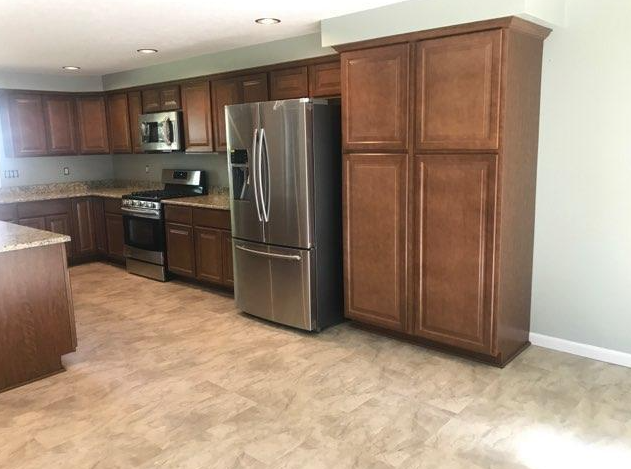 A kitchen with brown cabinets, stainless steel appliances, and beige flooring.