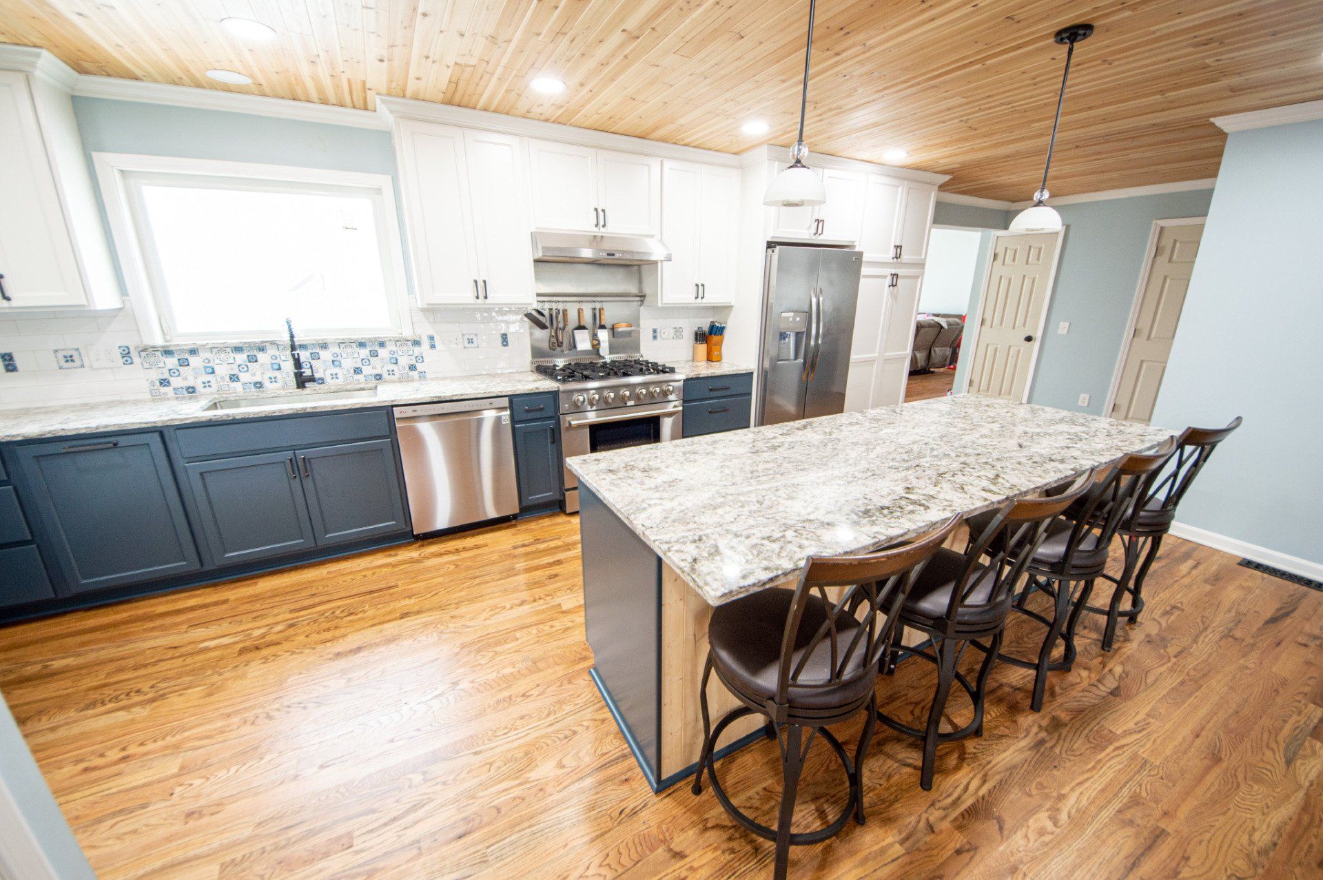 Kitchen with blue cabinets, granite countertops, wooden ceiling and floors, and island with bar stools.