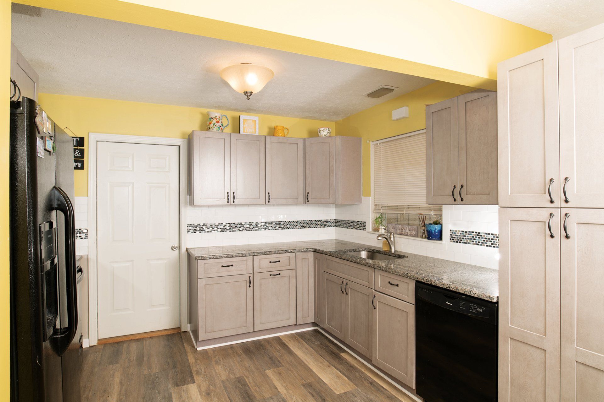 Kitchen with light gray cabinets, black appliances, yellow walls, and wood-look flooring.
