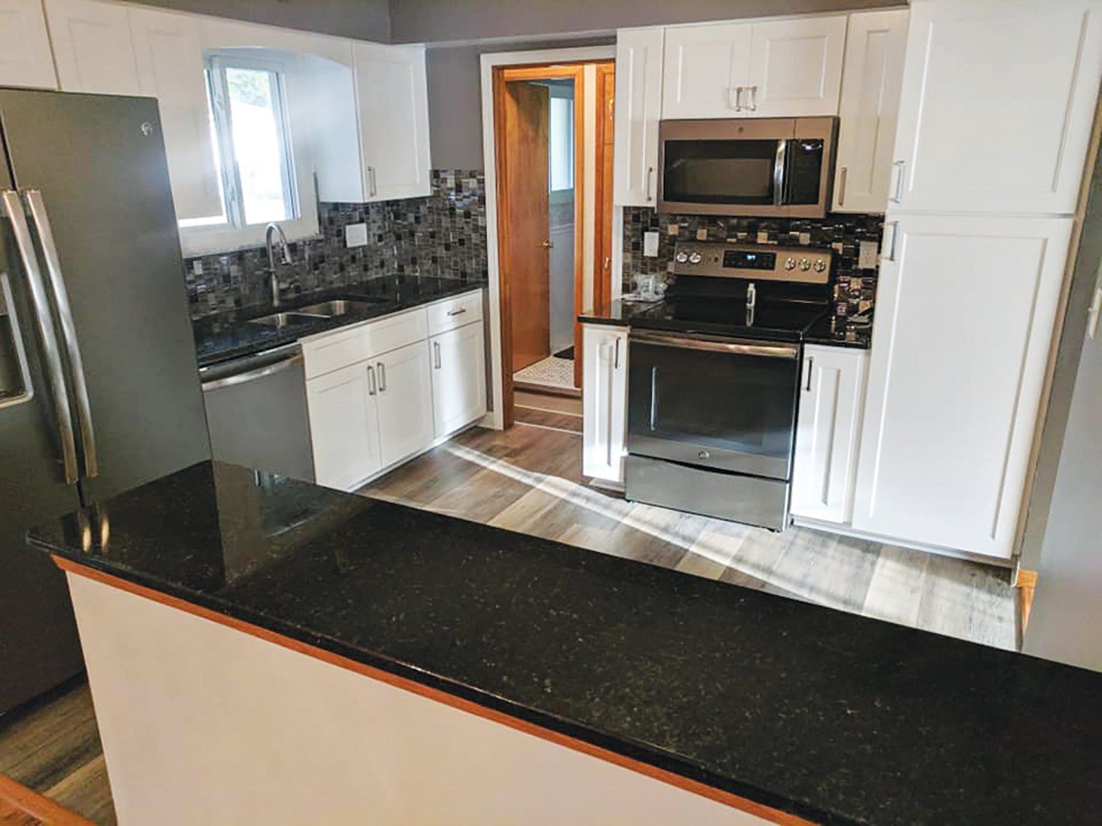 White kitchen with black countertops and backsplash, stainless steel appliances, and wood-look flooring.
