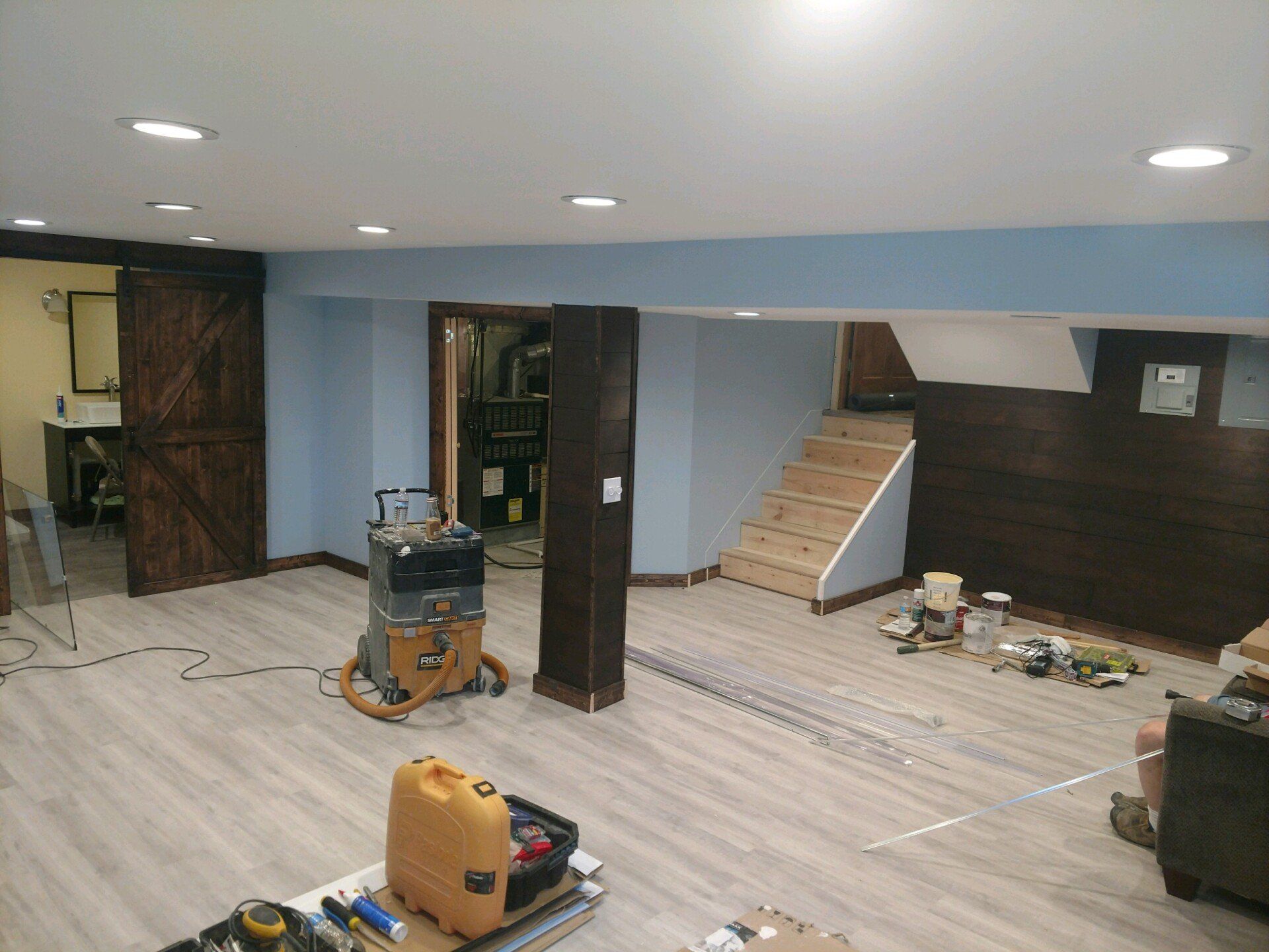 Basement renovation with new light wood flooring, blue and brown walls, stairs, and tools.
