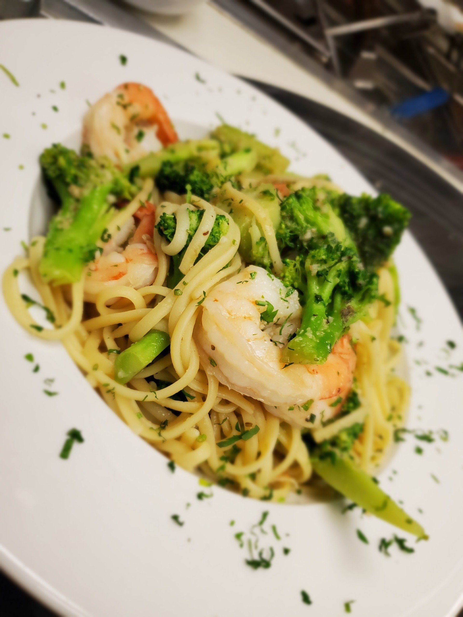 A white plate topped with noodles , broccoli and shrimp.