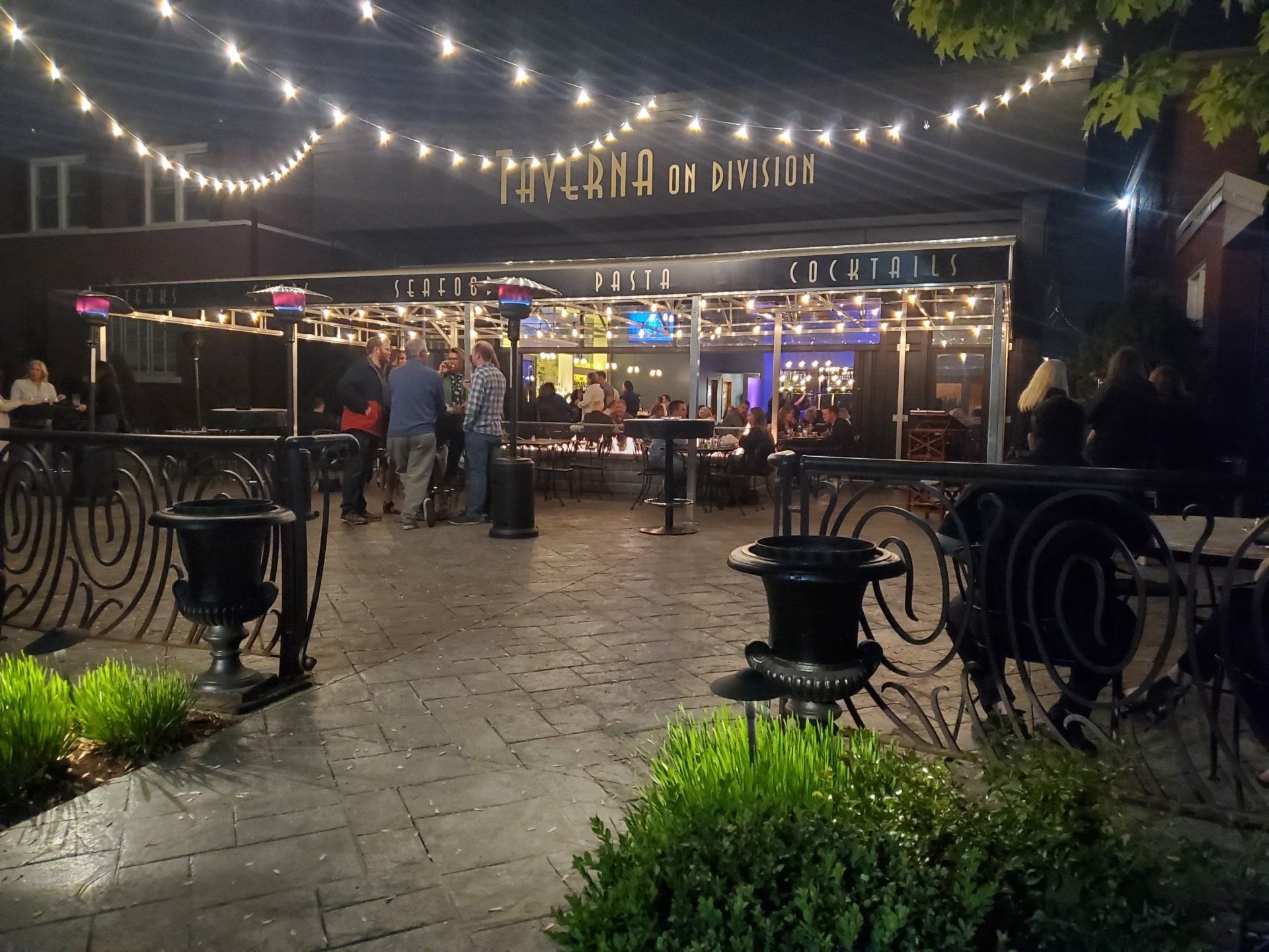 A group of people are gathered outside of a restaurant at night.