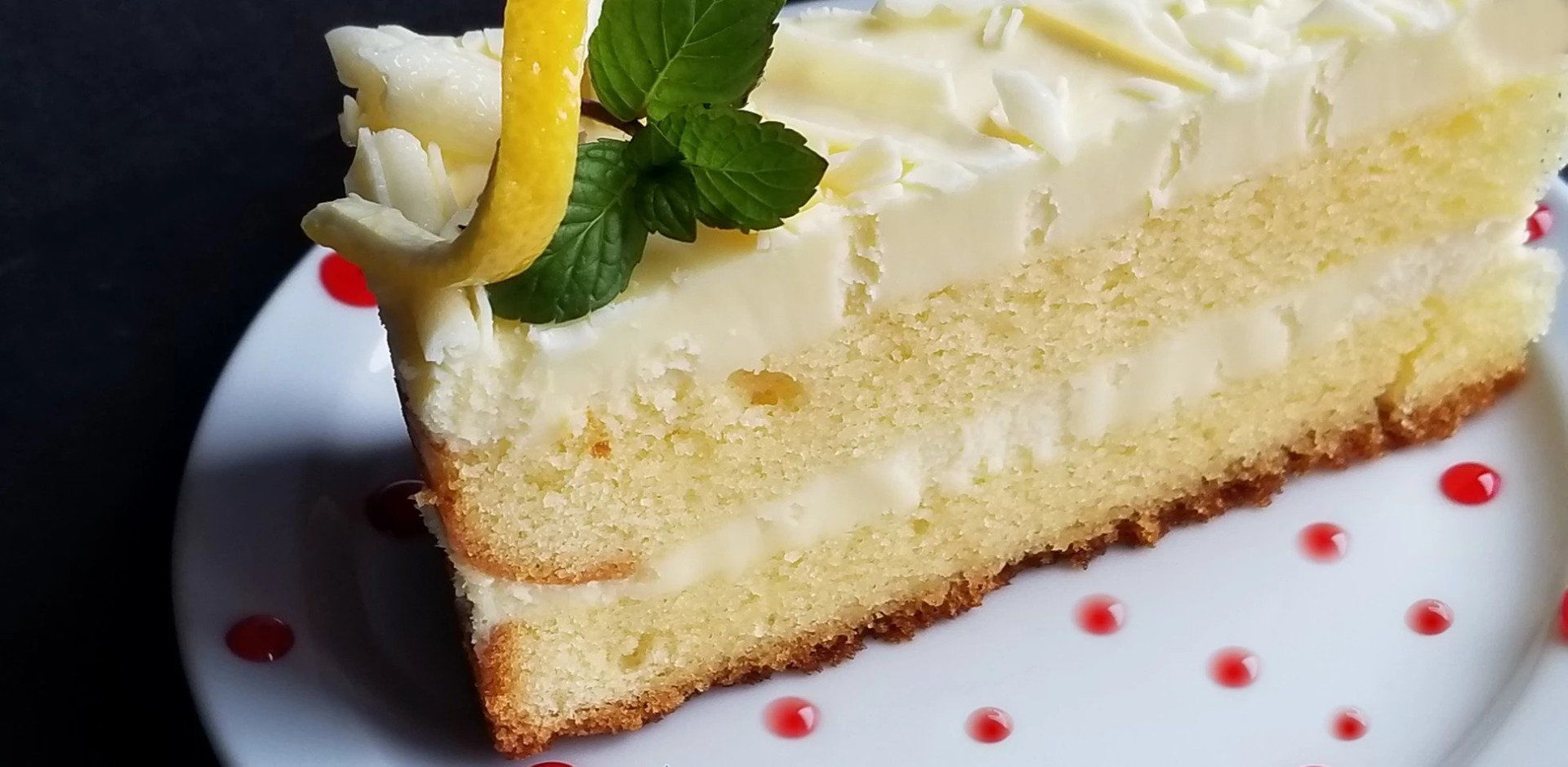 A slice of cake with a lemon slice on top is on a white plate.