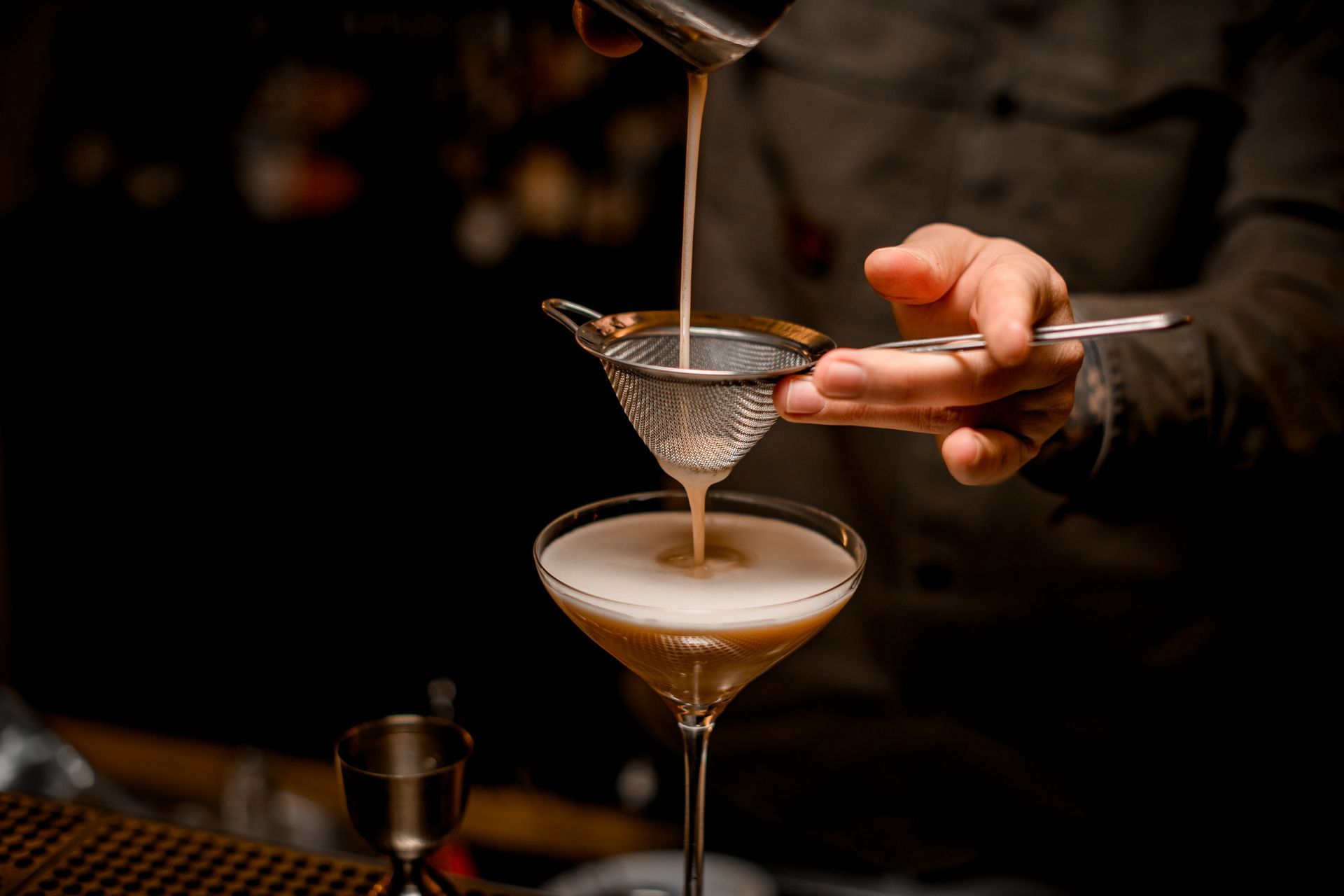 A bartender is pouring a drink into a martini glass.