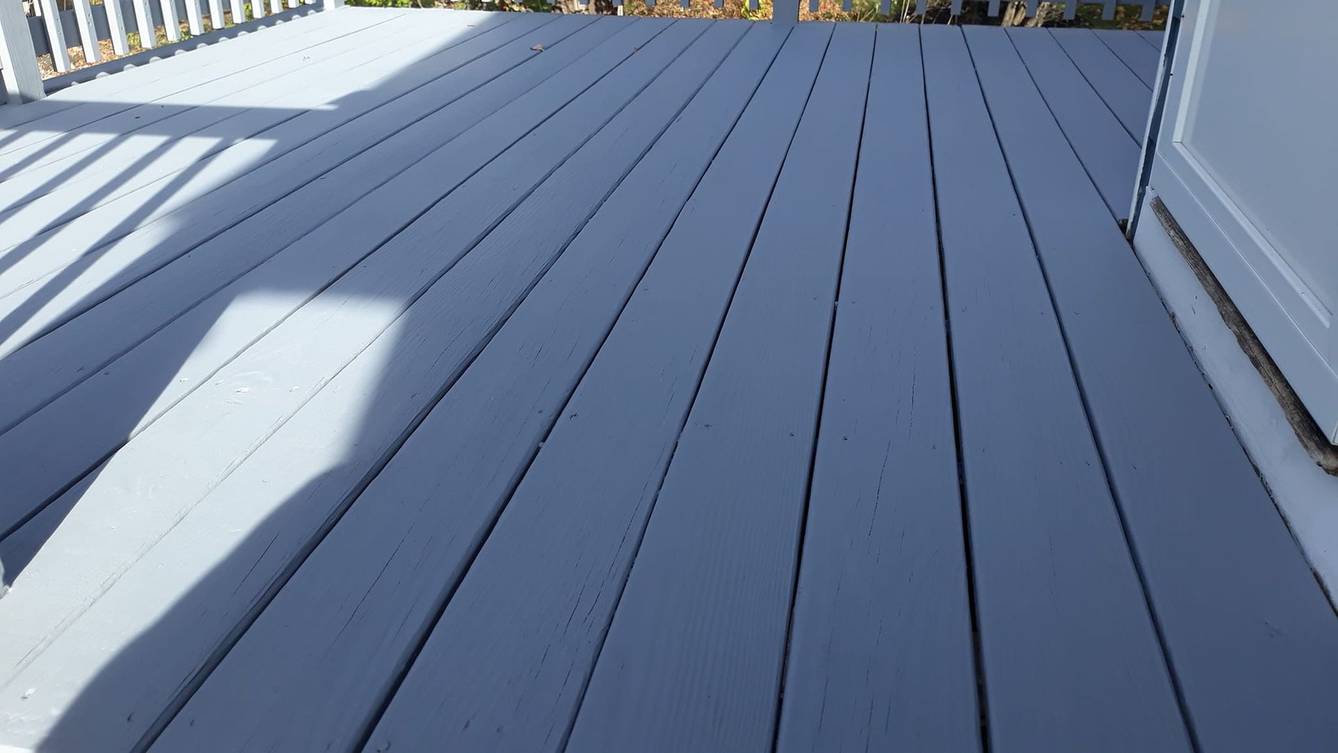 Gray wooden deck with white railing. Sunlight casts shadows.