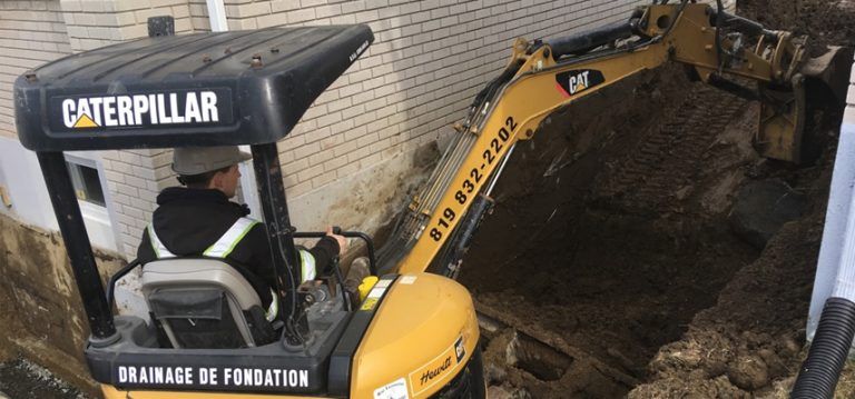 Un homme conduit une excavatrice à chenilles dans un trou.