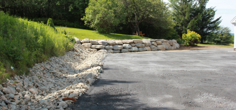 Une allée avec un mur de pierre sur le côté et des arbres en arrière-plan.