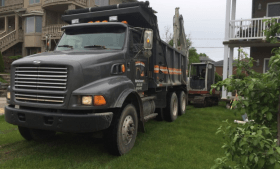 Un camion à benne basculante est garé dans l'herbe devant une maison.