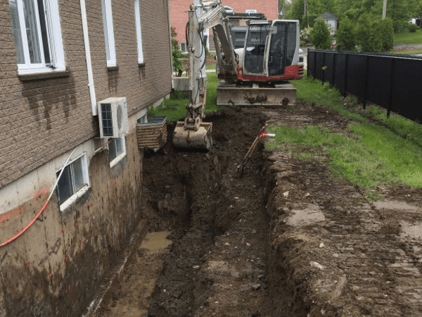 Une excavatrice creuse un trou devant un bâtiment en briques.