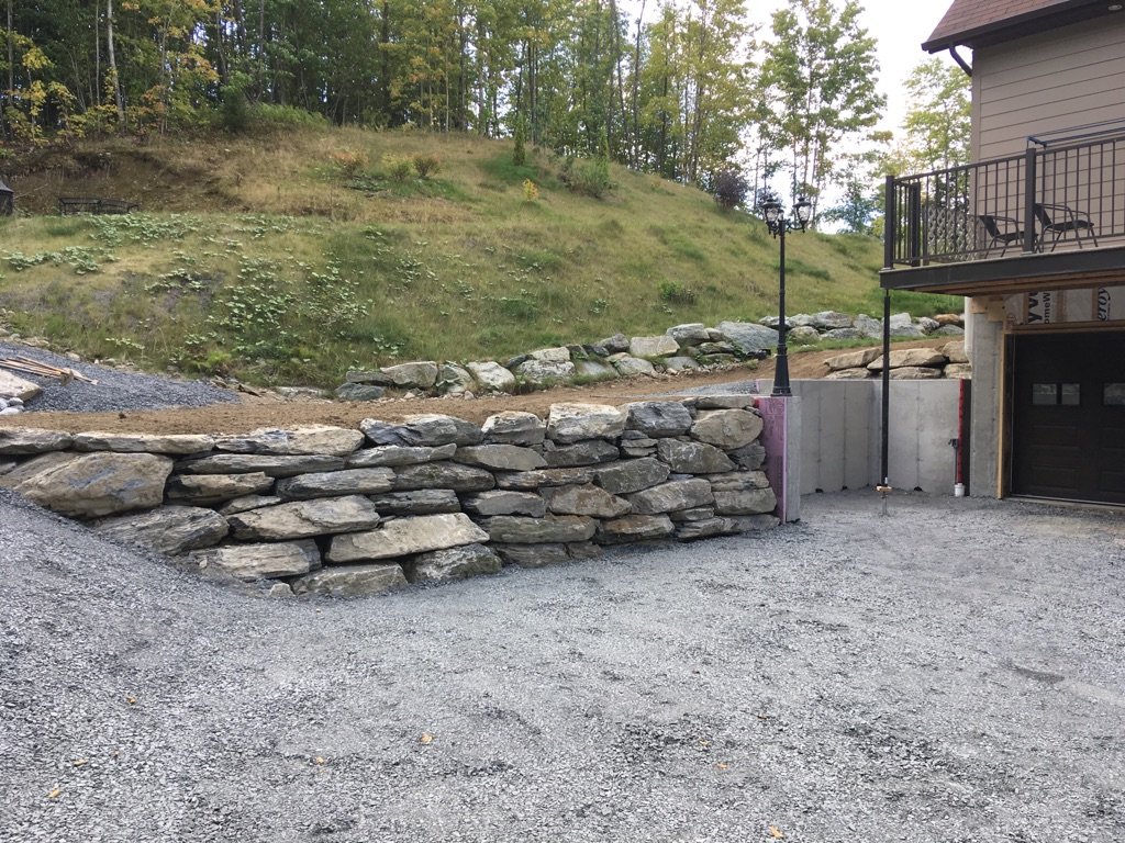 Un grand mur de pierre se trouve devant une maison.