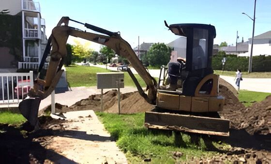 Une excavatrice creuse un trou dans le sol devant une maison.
