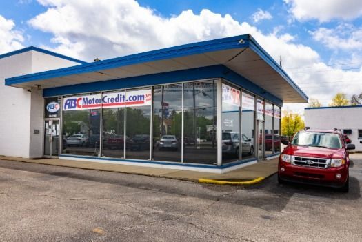 A red car is parked in front of a building that says autocredit.com