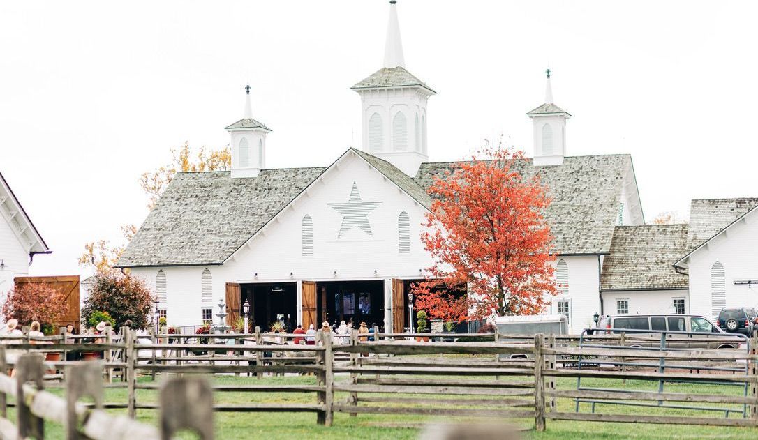 A large white barn with a wooden fence in front of it.