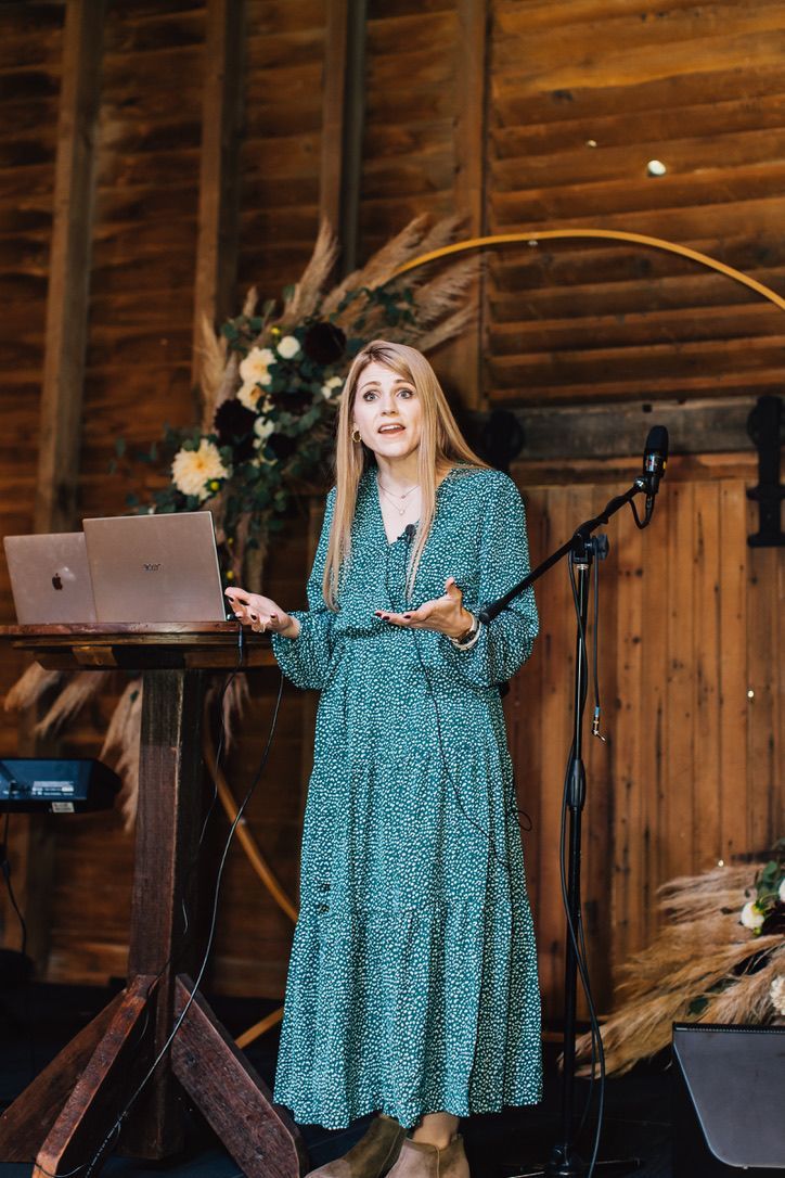 A woman in a green dress is standing in front of a microphone and a laptop.