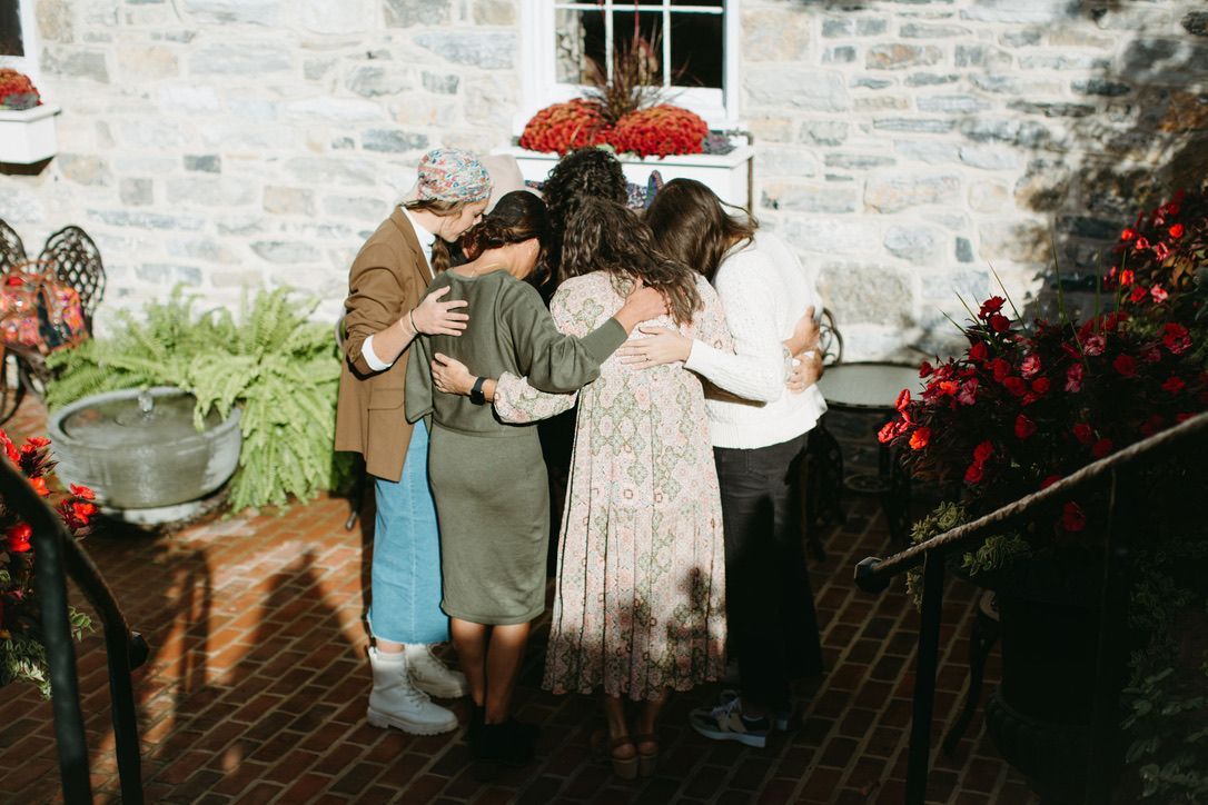 A group of women are standing in a circle hugging each other in front of a stone building.