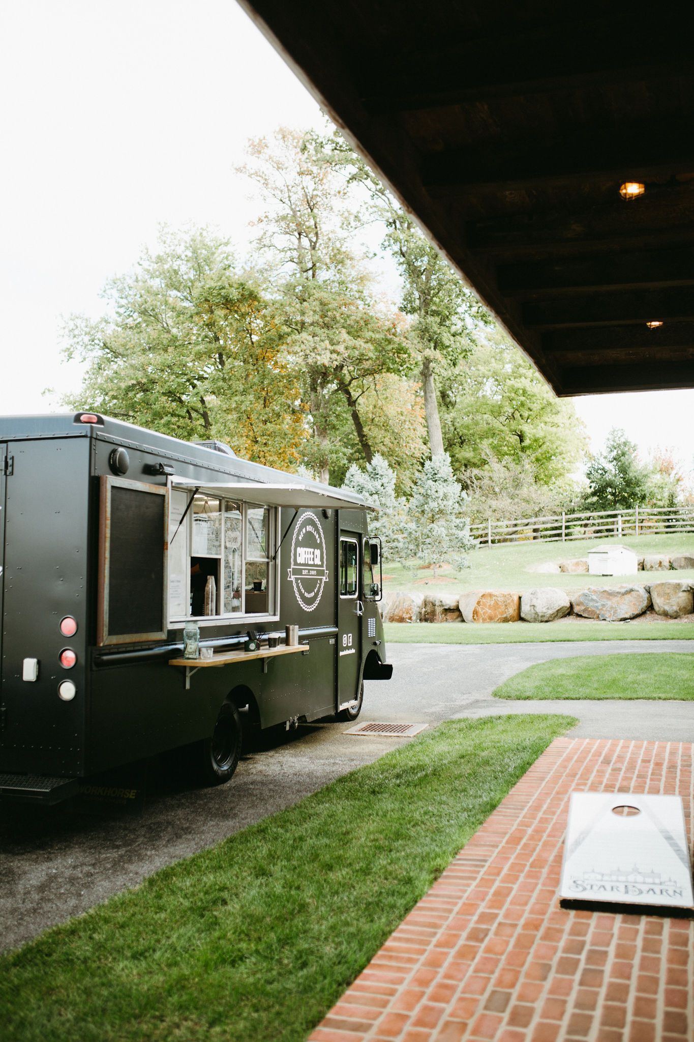 A food truck is parked in the grass next to a brick walkway.