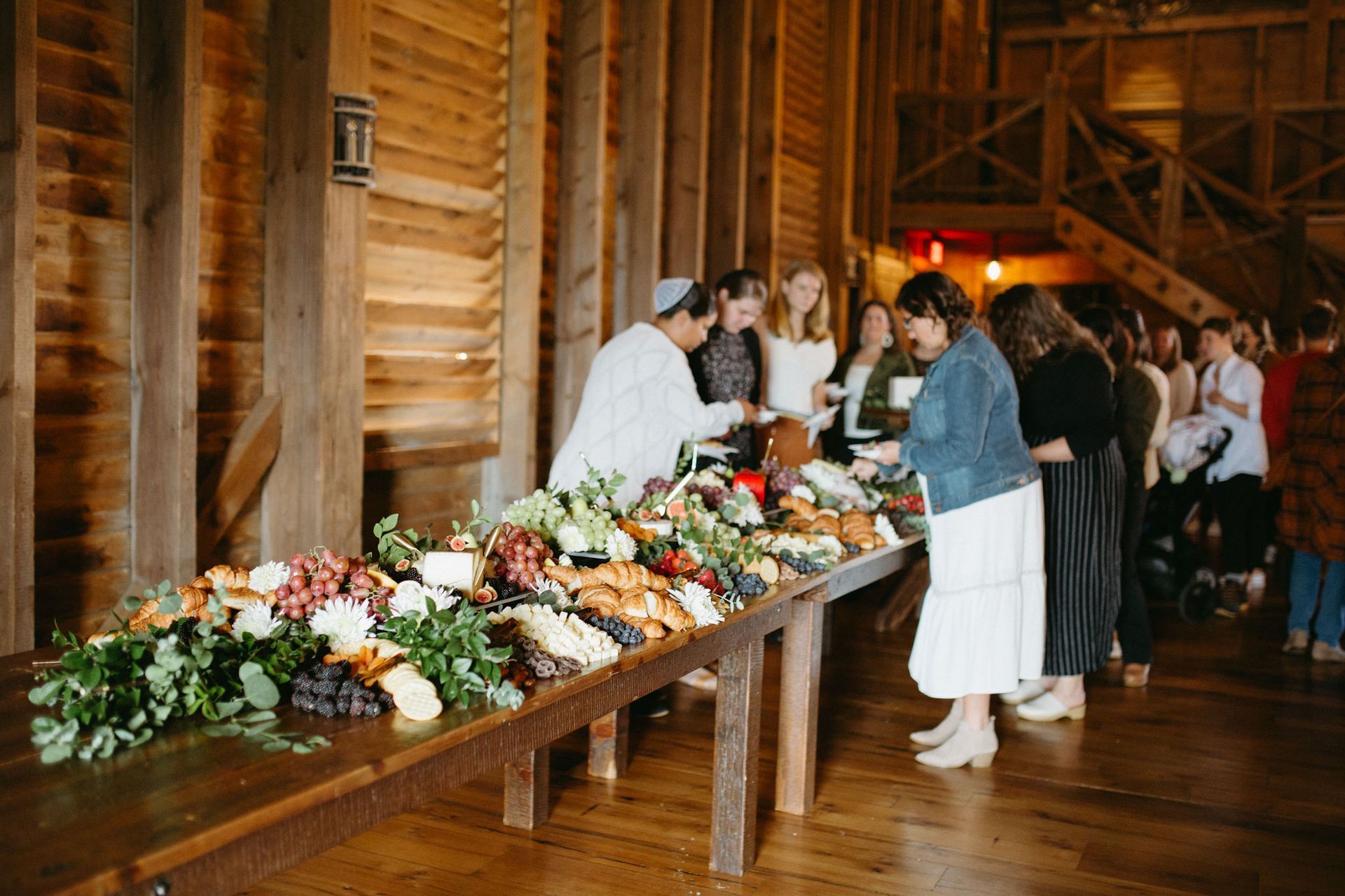 A group of people are standing around a buffet table in a barn.