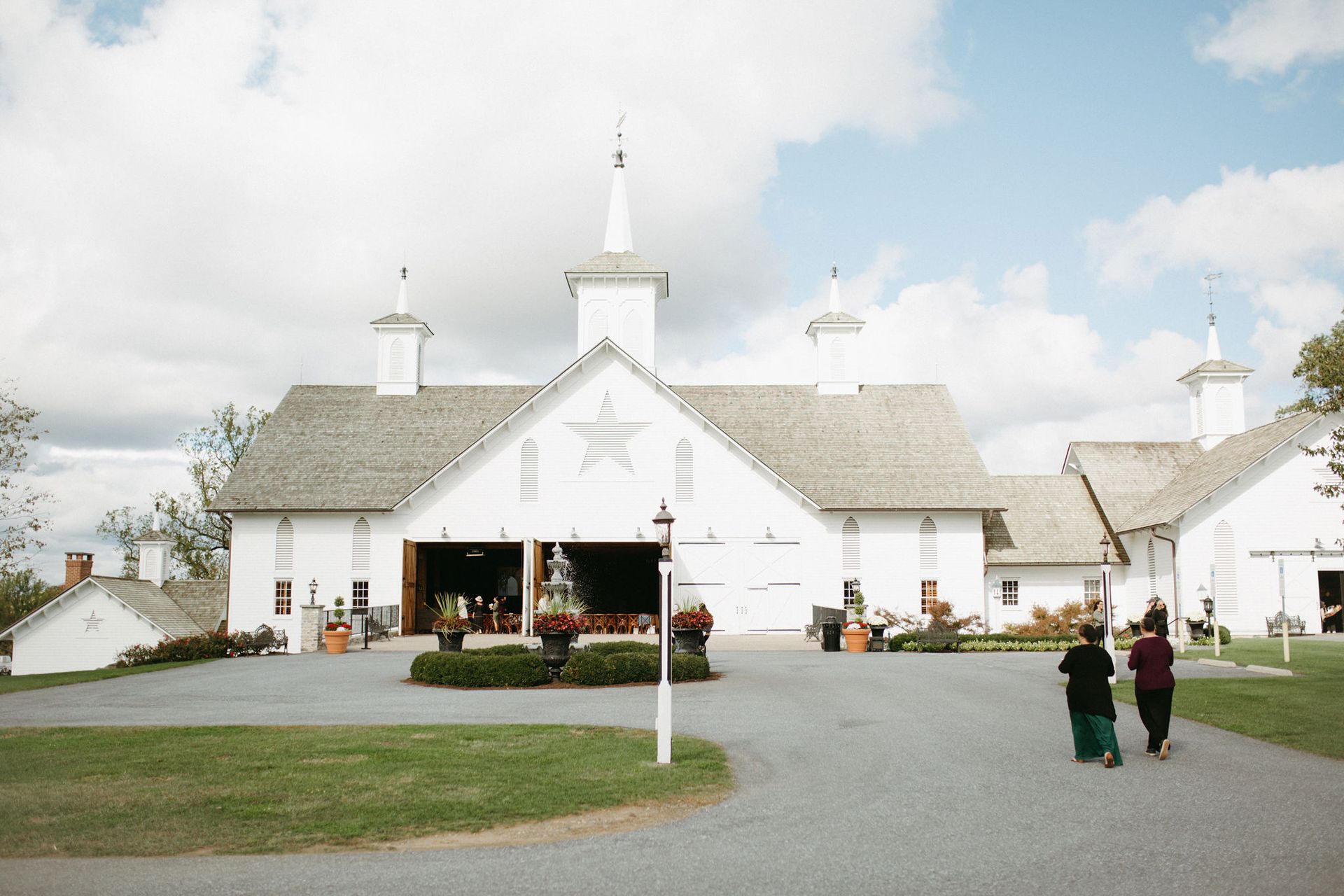 Two people are walking in front of a large white barn.