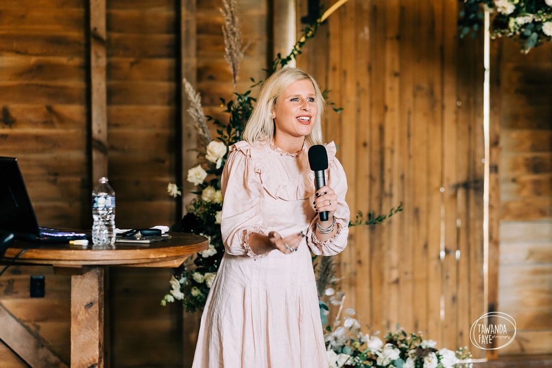 A woman is standing in front of a wooden wall holding a microphone.