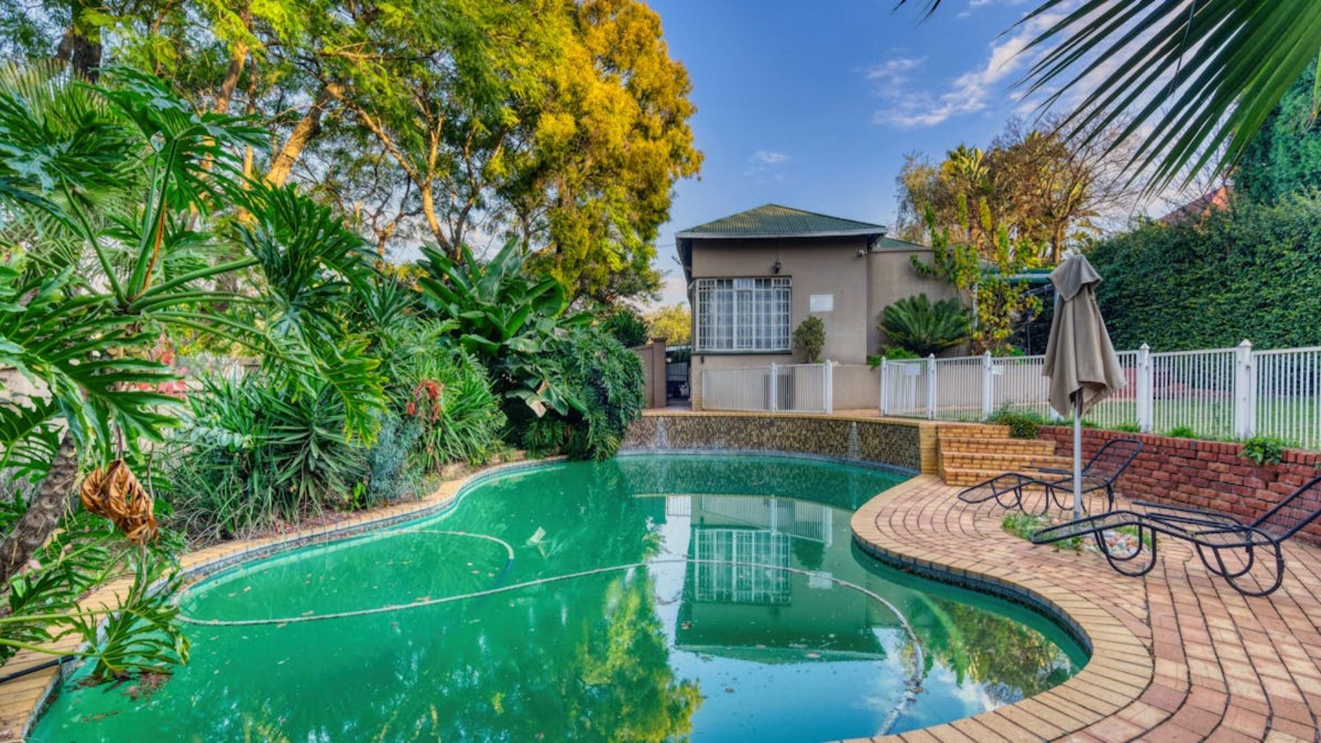 Piscina en un exuberante patio trasero con una casa al fondo.