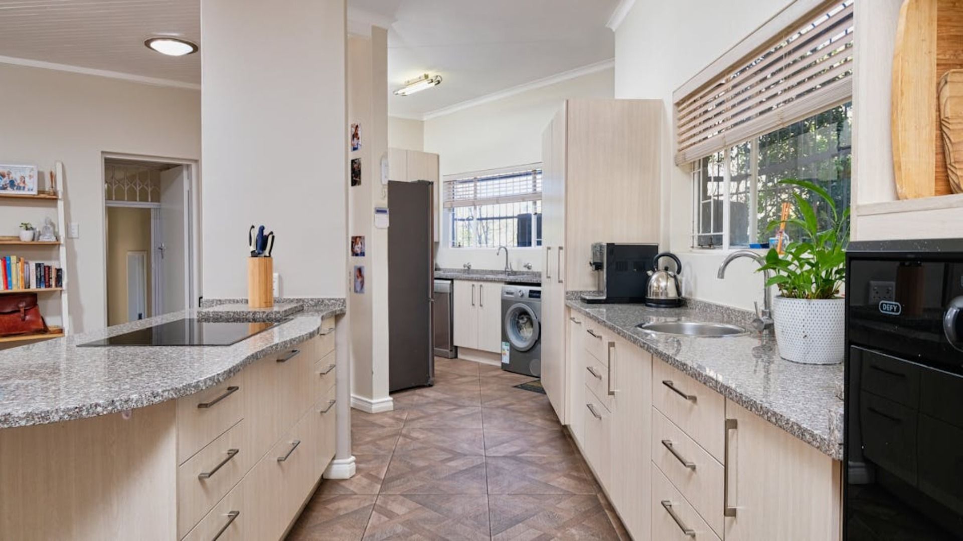 Cocina con gabinetes de madera clara, encimeras de granito, electrodomésticos de acero inoxidable y una ventana.