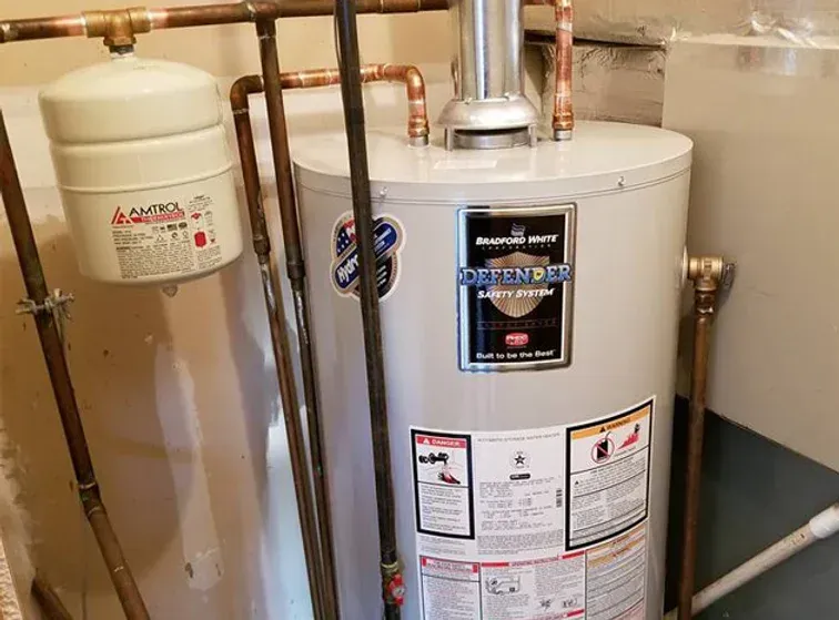A water heater is sitting in a basement next to copper pipes.