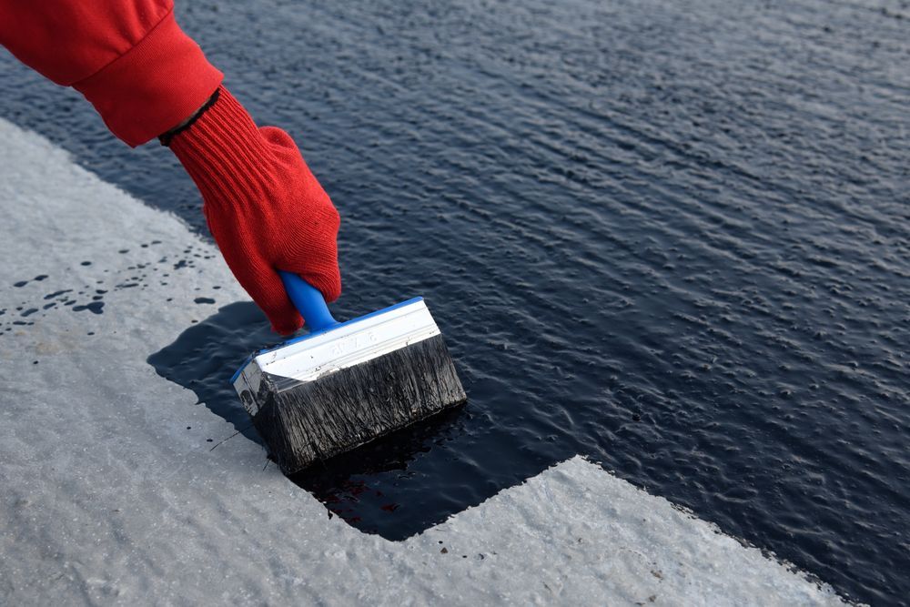 Hand With Red Glove Applying Black Sealant With Brush to a Surface — 1 Time Waterproofing In East Ballina, NSW