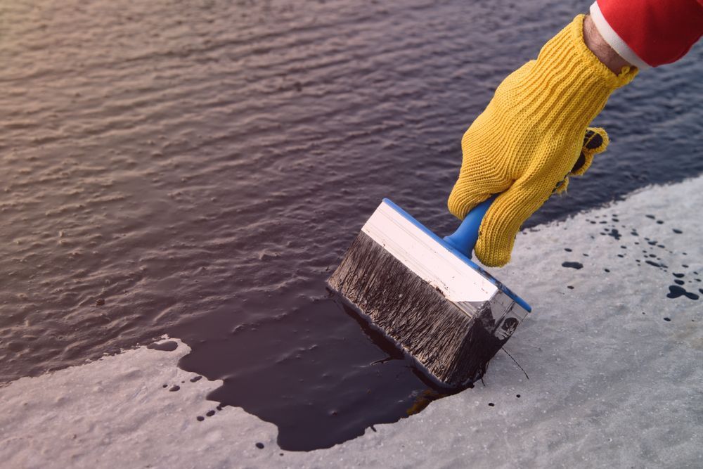 Hand in Yellow Glove Using Brush to Apply Black Sealant on a Surface — 1 Time Waterproofing In Tweed Heads, NSW