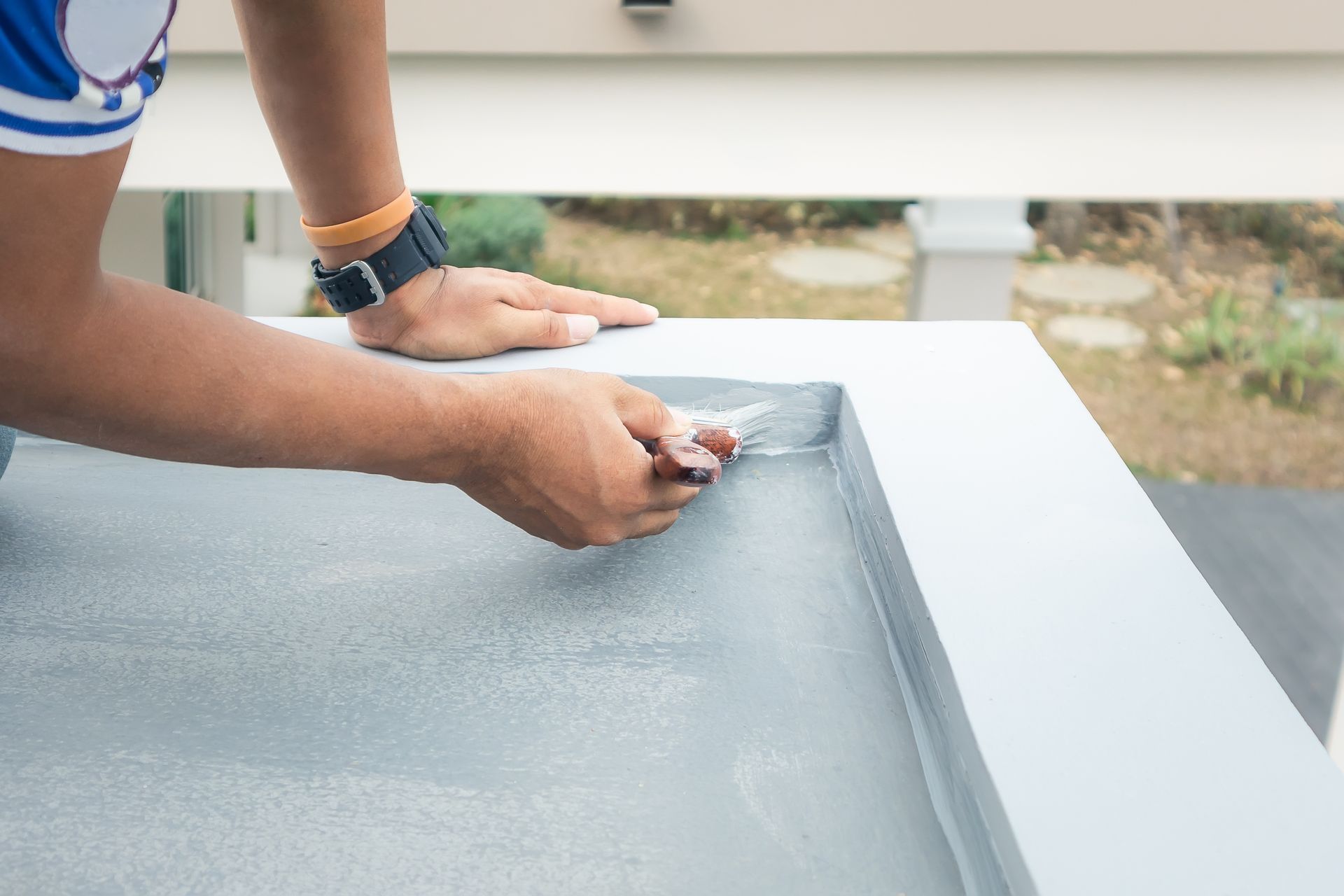 Person Applying Sealant to a Gray Surface With a Putty Knife Outdoors — 1 Time Waterproofing In East Ballina, NSW