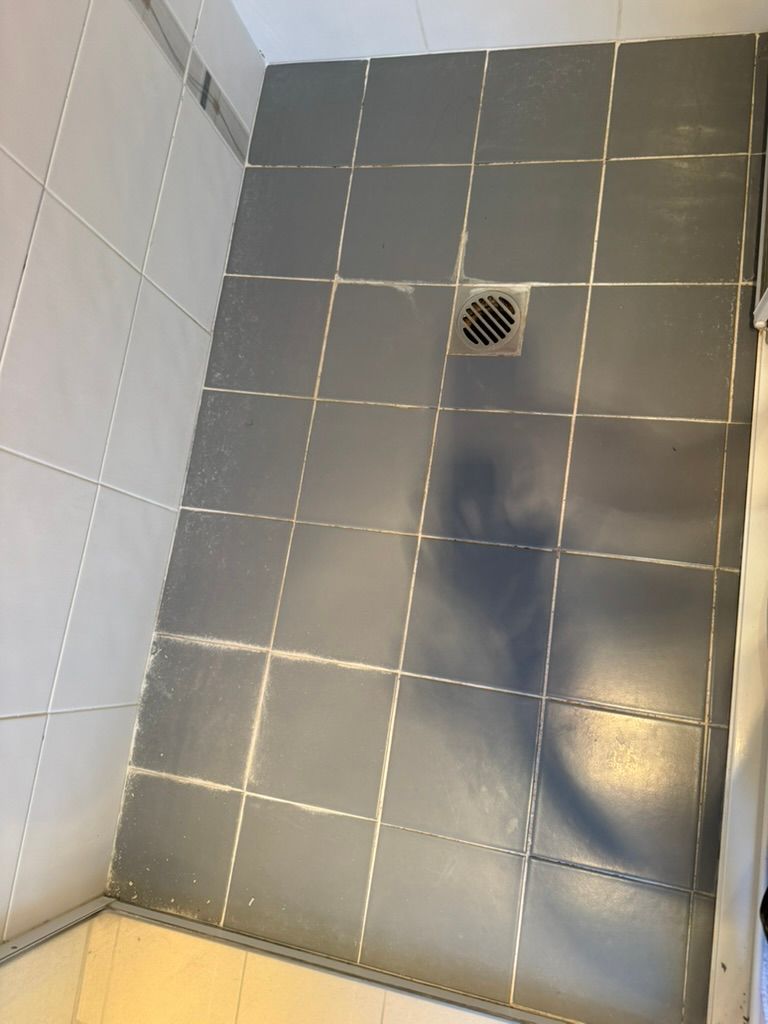 Shower floor tiled with grey squares, drain visible. White tiled walls.
