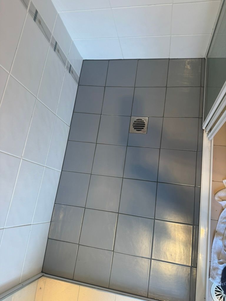 Gray tiled shower floor with drain, surrounded by white and gray tiles.