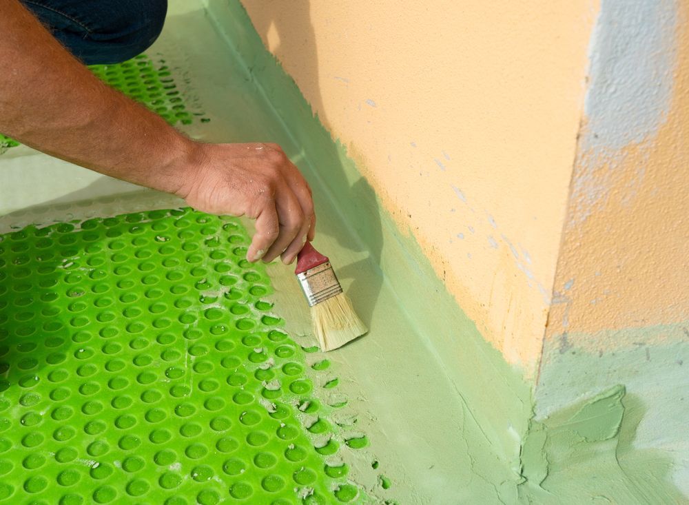 Person Using a Brush to Apply Sealant to a Green, Dimpled Membrane in a Corner — 1 Time Waterproofing In Lismore, NSW