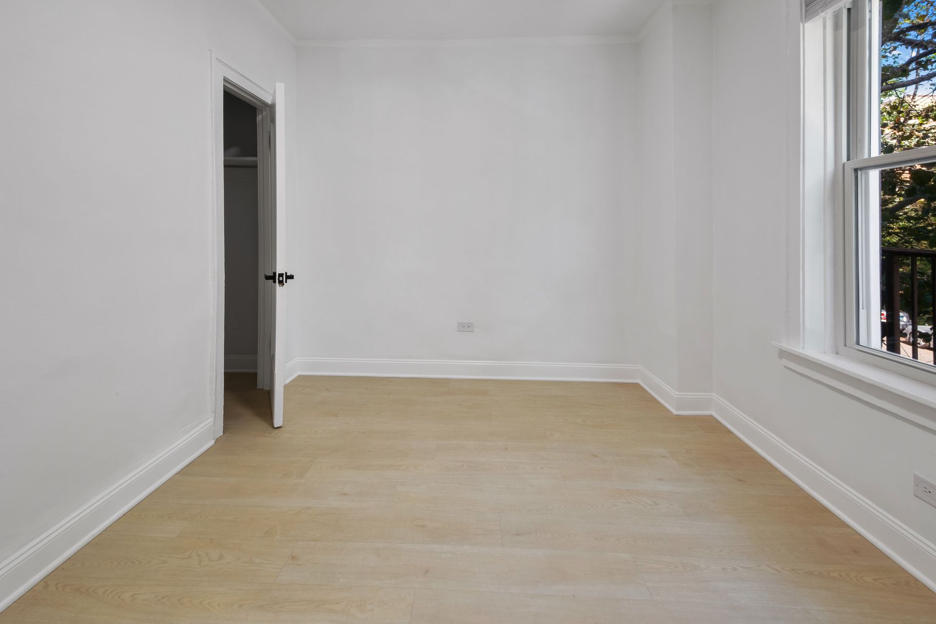 Empty room with light wood floor, white walls, and a window.
