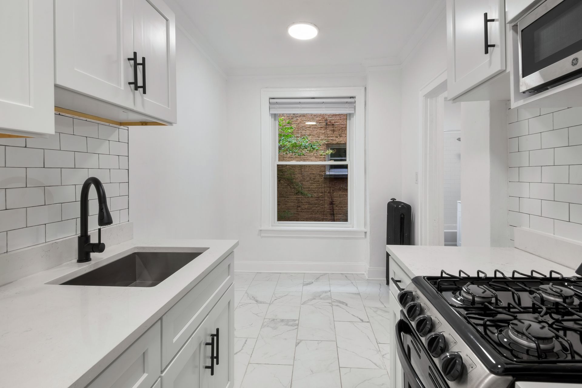Bright white kitchen with black accents, including a gas stove, sink, and cabinets.