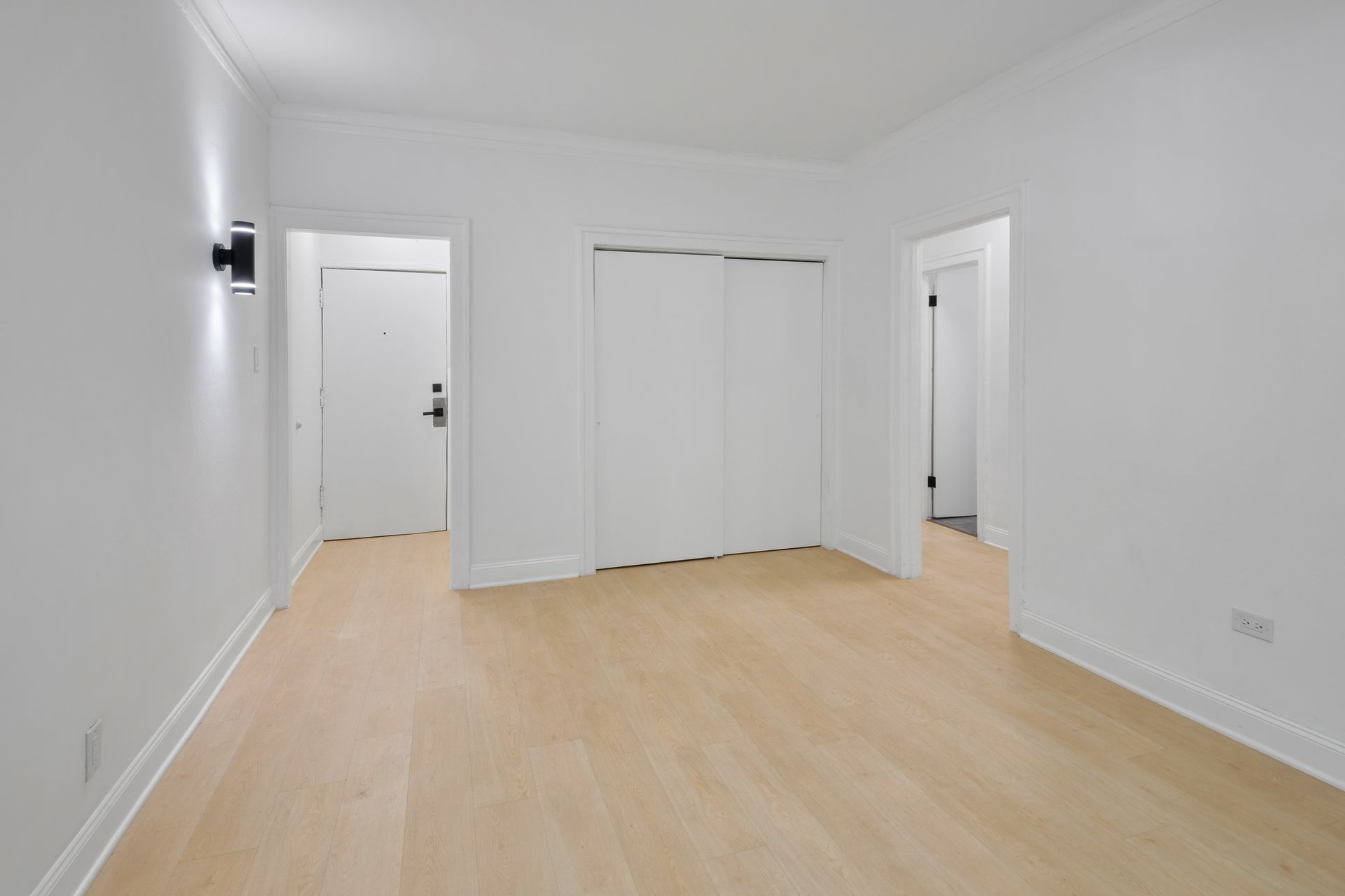 Empty room with light wood floors, white walls, and three white doors.